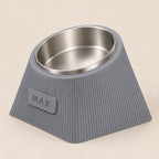 Contour Tilt custom height dog bowl in Ash Grey, with a tilted stainless steel bowl, fine vertical grooves and MAX example nameplate.